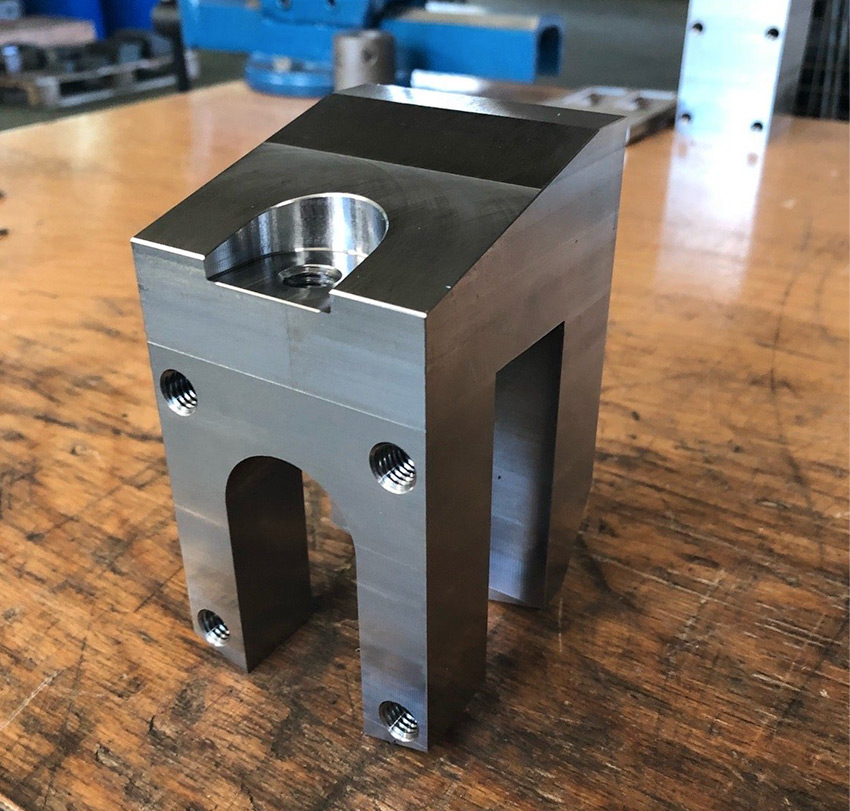 Ein exakt gefrästes Werkstück mit komplizierten Öffnungen und Aussparungen steht auf einem Tisch.