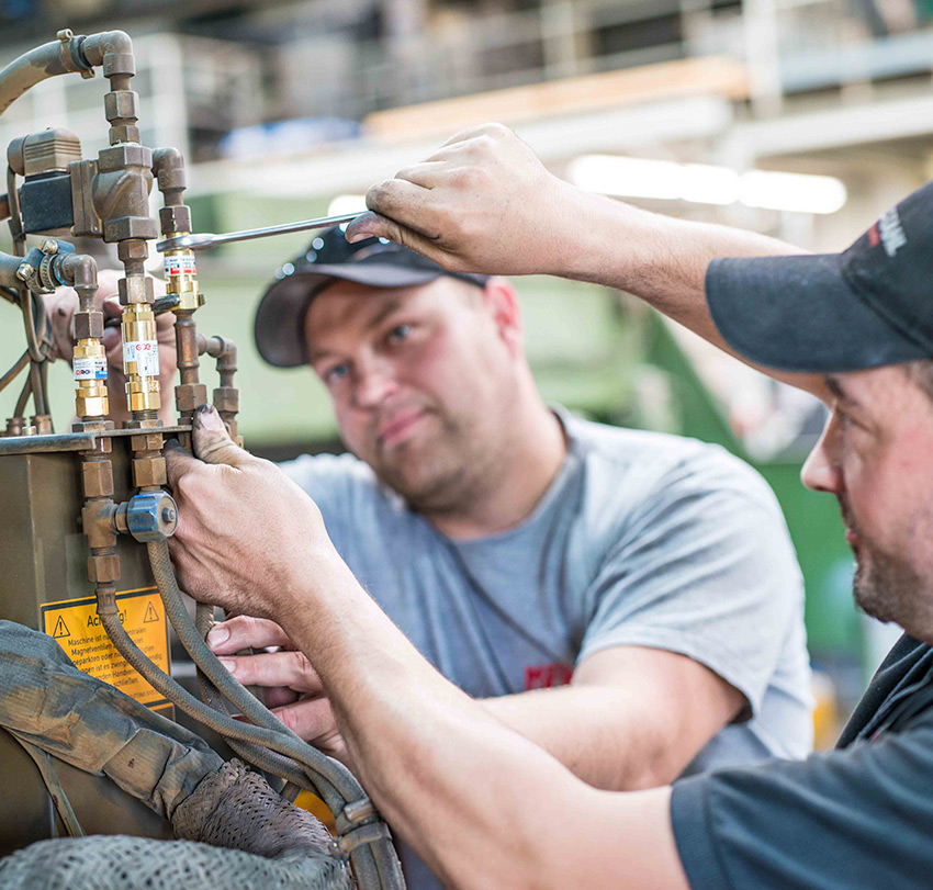 Zwei Mitarbeiter reparieren die Schlauchverbindungen einer Maschine.
